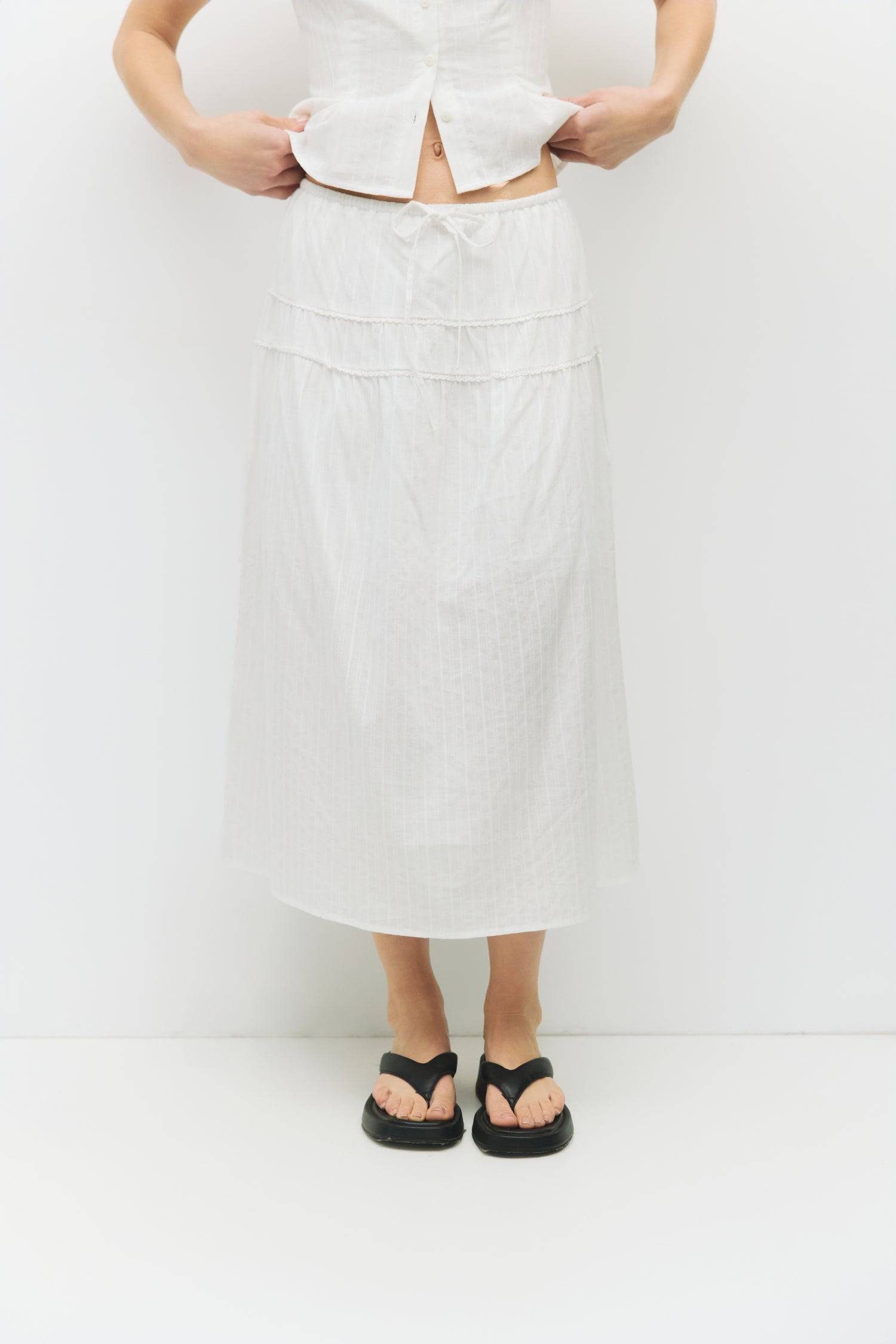 8983694868701, The Keaton Skirt, Bottoms, All Row, Black,Bottom,Bottoms,Casual,cf-color-black,cf-color-cream,cf-size-l,cf-size-m,cf-size-s,cf-vendor-mod-ref,Comfortable,Cotton,Cream,curve skirt,drawstring waist,Dress,Everyday,final-sale,finalsale,Form Fitting,Linen,linen-blend,maxi skirt,Midi Dress,midi length,new,Rib Knit,Ribbed,sale,Sleeveless,Spring,Summer,womens, Information The Keaton Skirt is a midi-length skirt with an elasticized waistband and adjustable ties. Finished with delicate lace trim and a