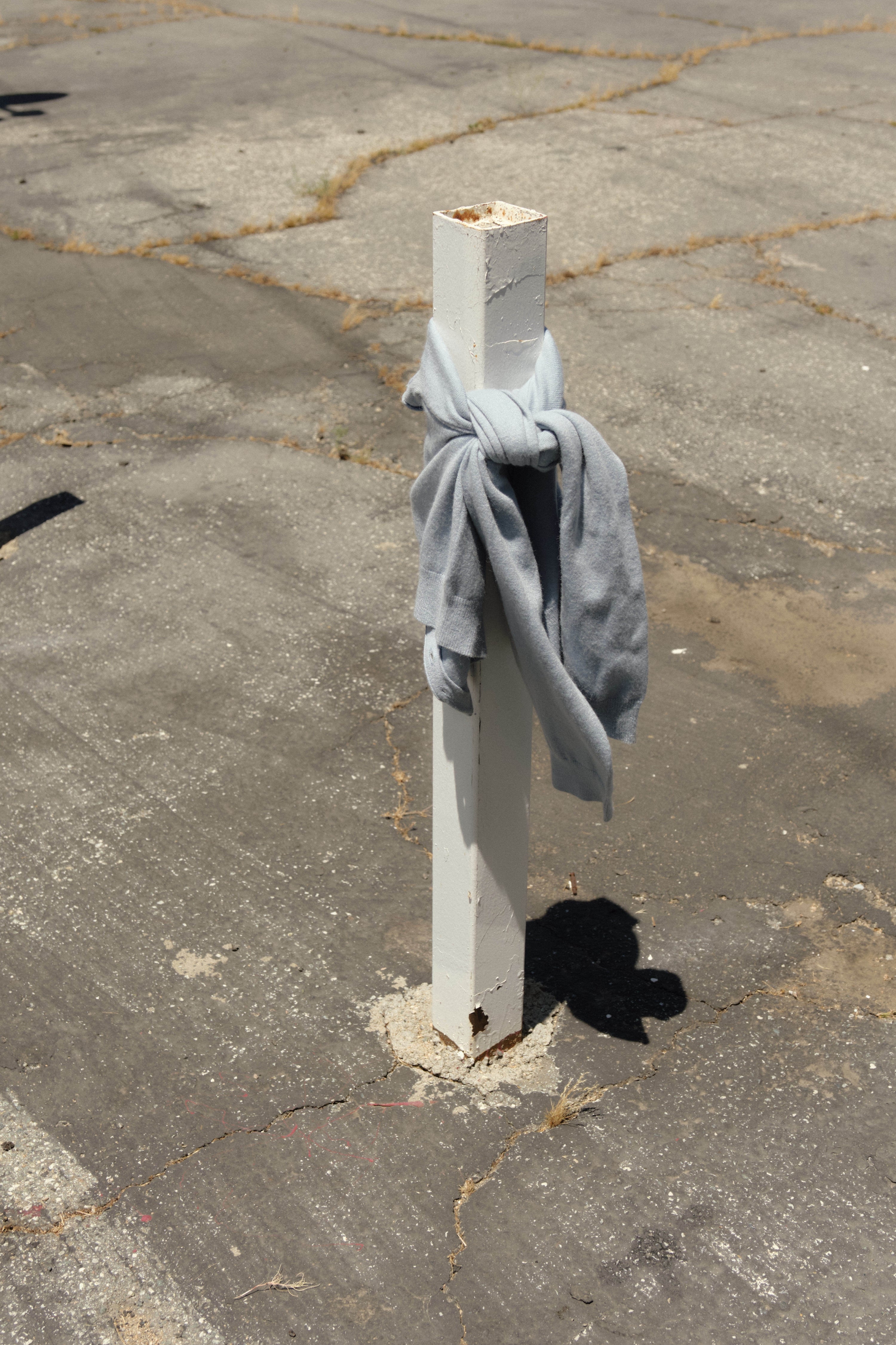 Light gray sweater casually tied around a white wooden post, standing on a weathered, cracked pavement in an outdoor setting.