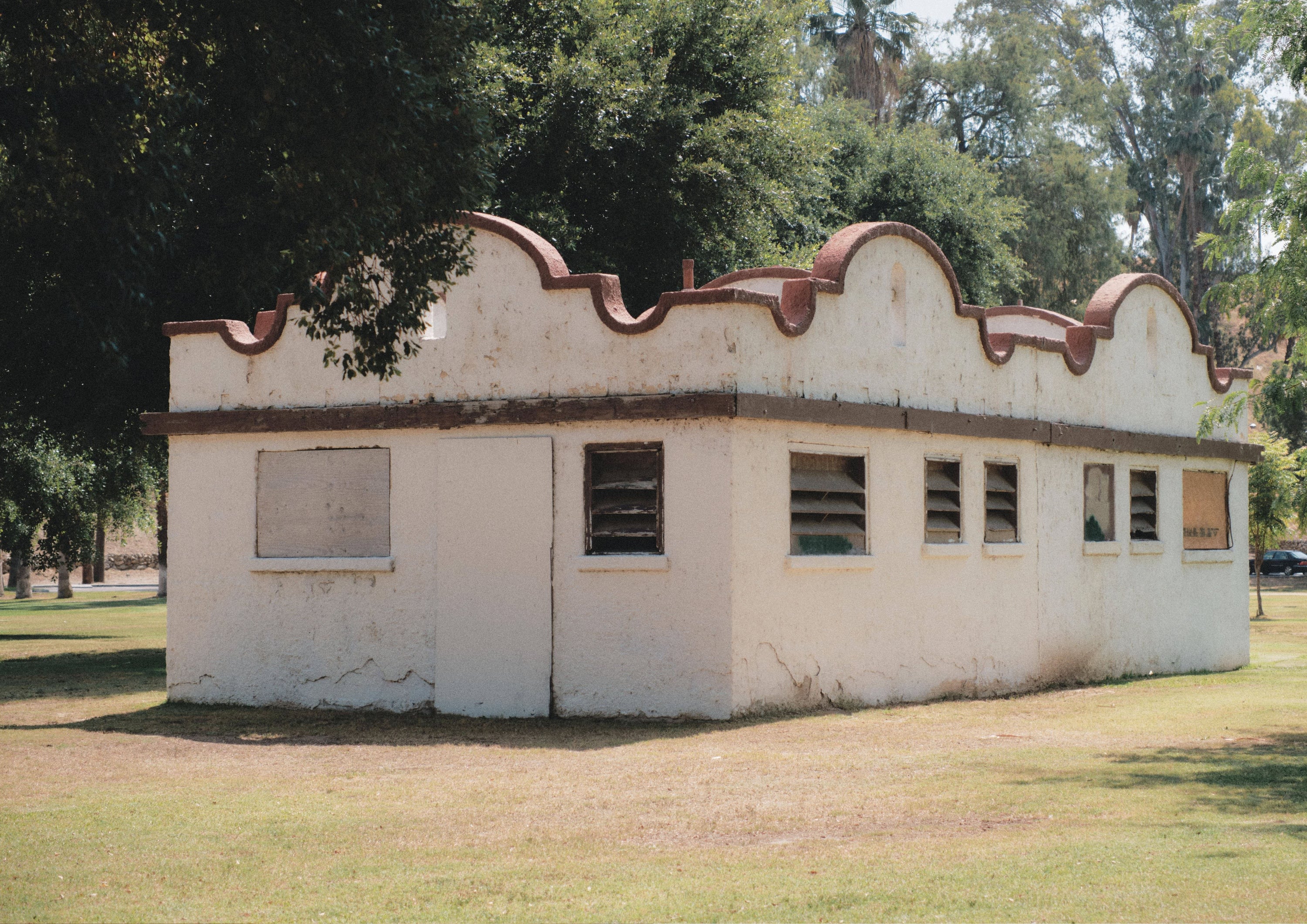 Landscape photo of a white adobe-style wall with organic curves and tall trees in the background. Evokes stillness and natural beauty.