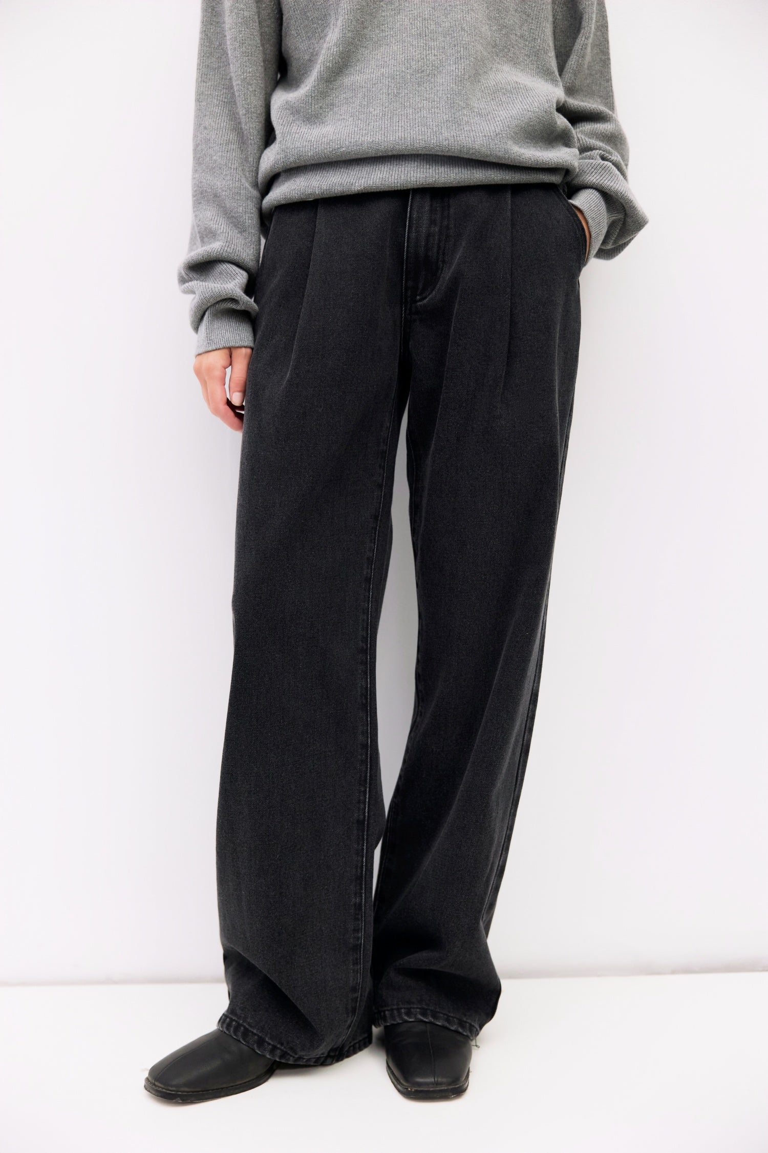 Person wearing black wide-leg pants and a gray sweatshirt against a white background