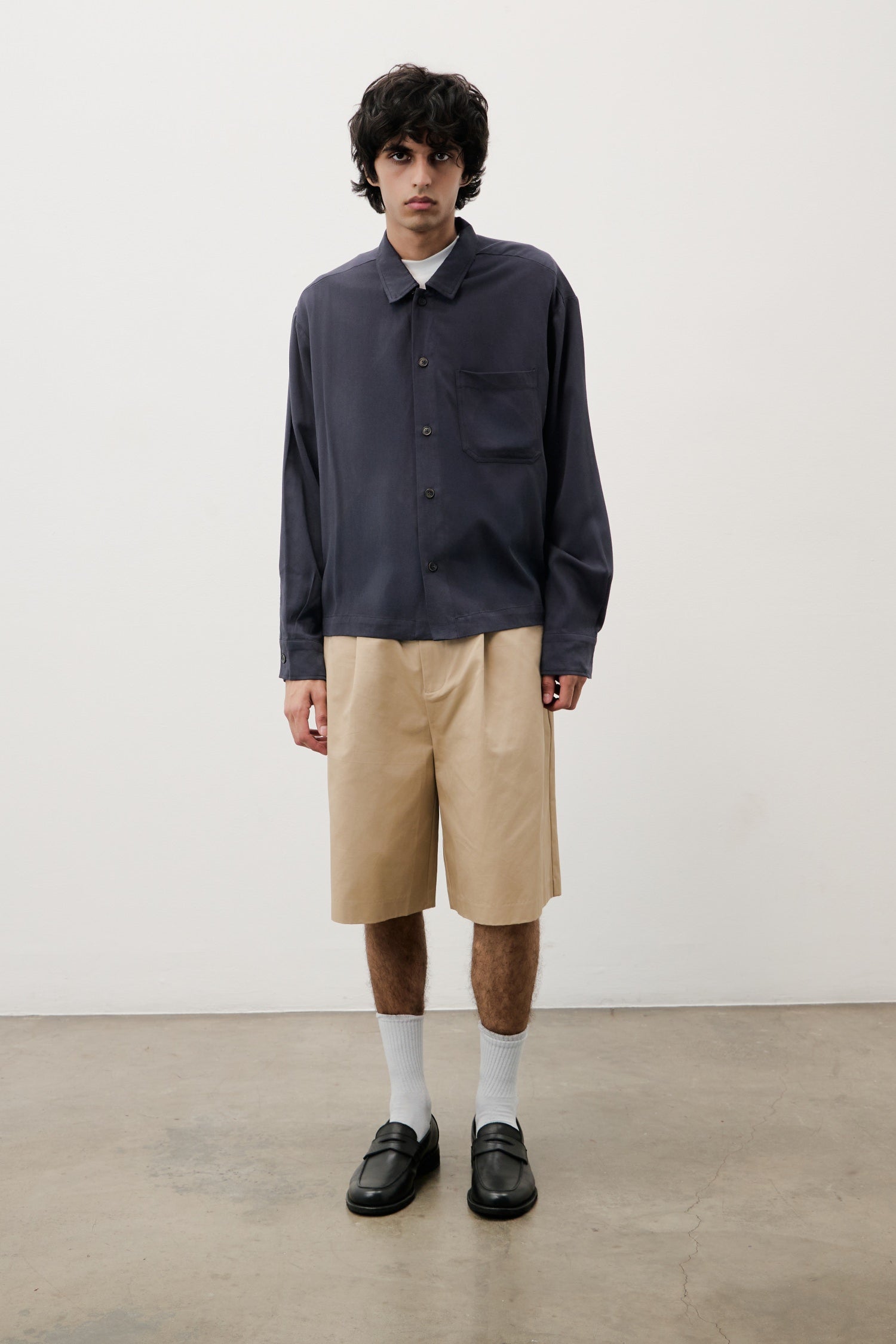 Person wearing a dark shirt and beige shorts against a white background
