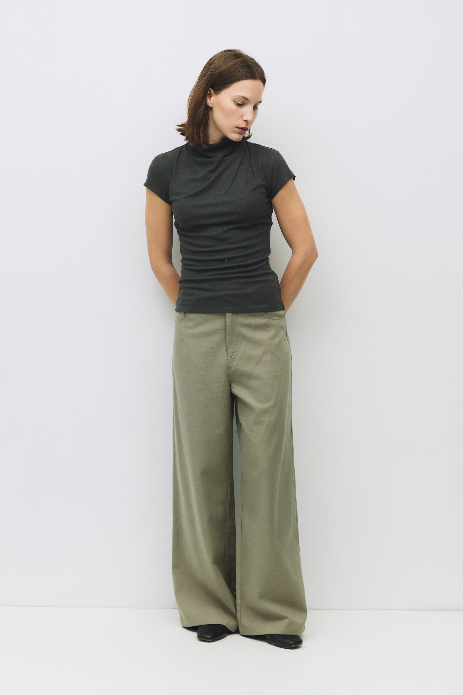 Model is wearing a charcoal form fitting rib knit mock neck top, front view. 