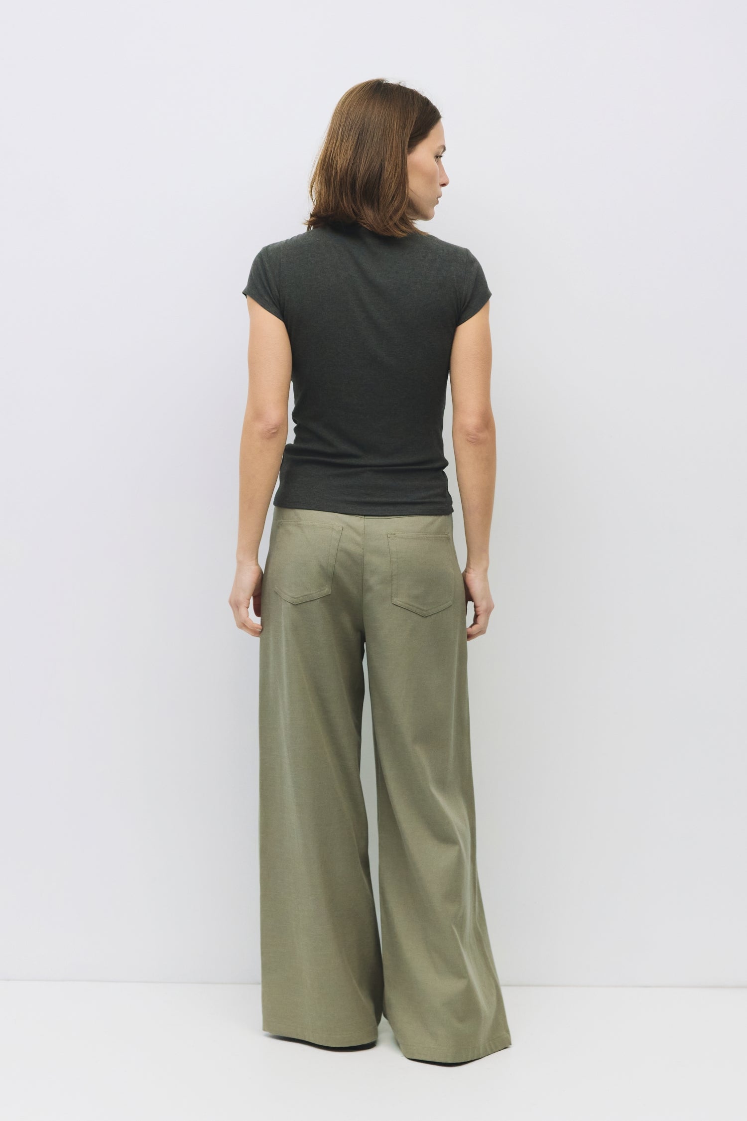 Model is wearing a charcoal form fitting rib knit mock neck top, back view. 