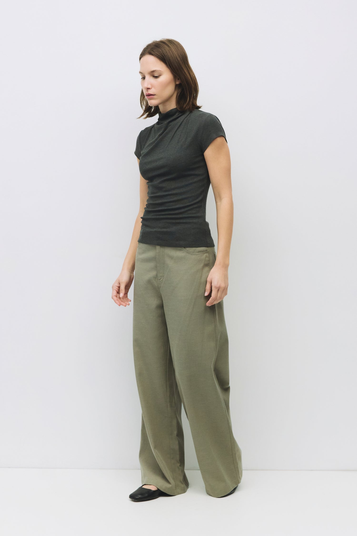Model is wearing a charcoal form fitting rib knit mock neck top, side view.